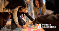 A group of people are gathered on the floor, leaning in and collaborating as they arrange colorful sticky notes. The scene is active and focused. The Mozilla Foundation logo appears in the bottom right corner.